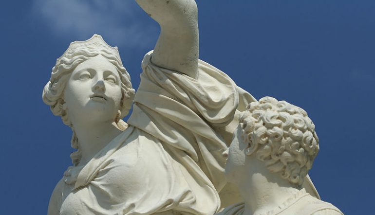 white statue of Ino with her son looking up at her, against a blue sky