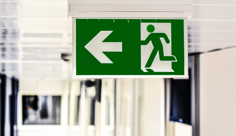 green exit sign above a door features a large arrow and a figure following it 