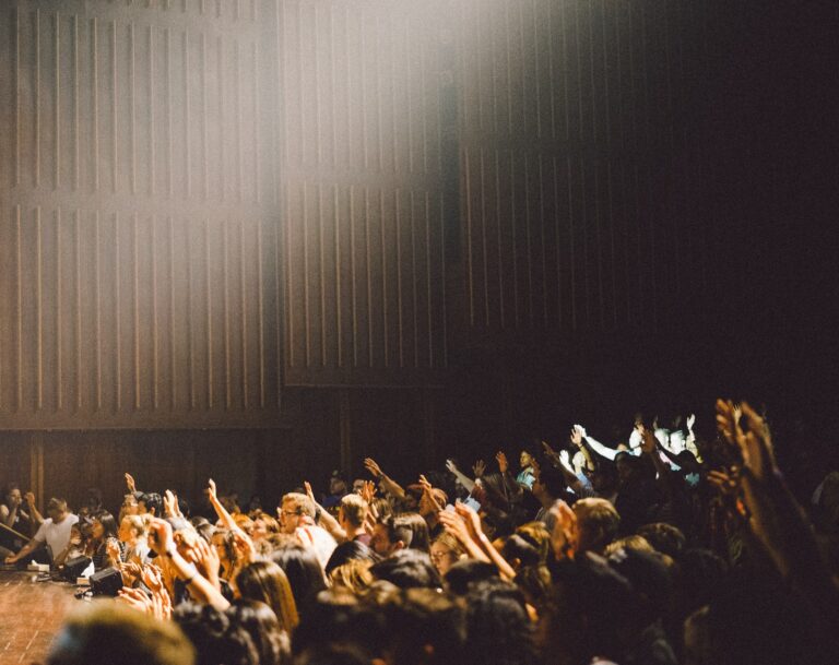 In a dark lecture hall, students raise their hands and light filters in from above.