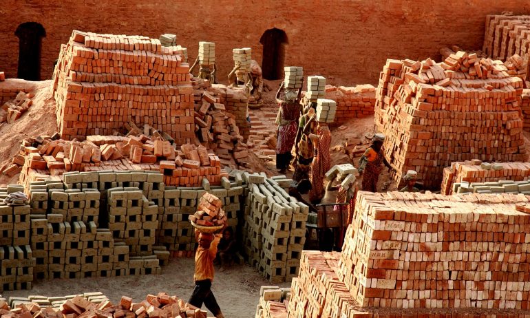 Bangladeshi women working among rows of bricks and cinderblocks - the women carry the cinderblocks and bricks above their heads