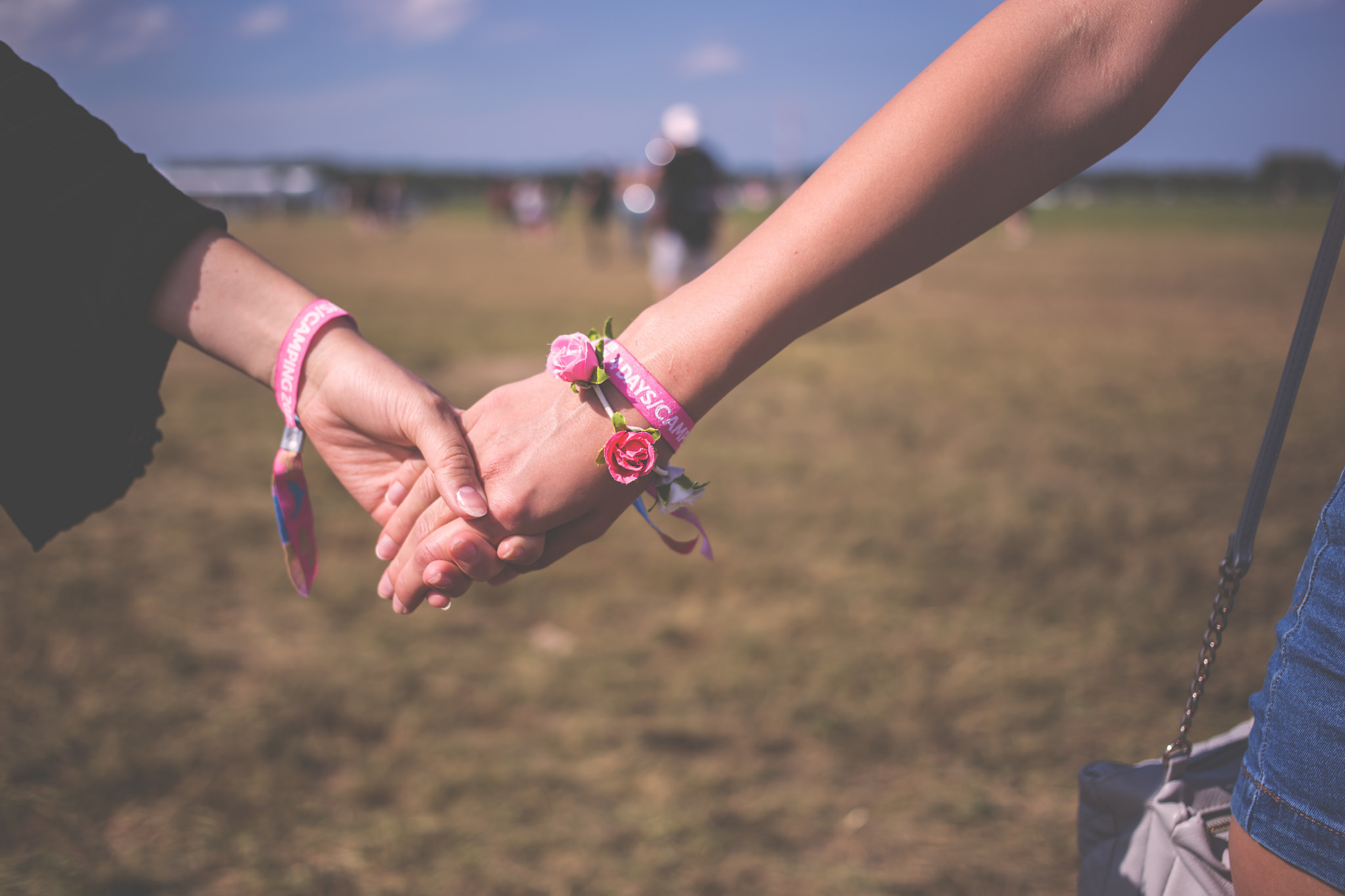 Two people holding hands wearing the same bracelets, one wears a bracelet made of small, fake roses
