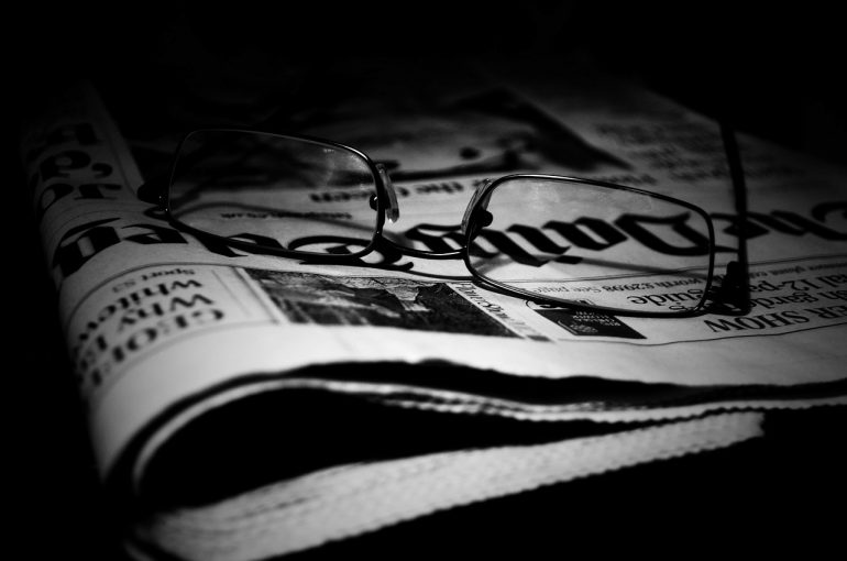 Black and white photograph of glasses sitting on a folded newspaper