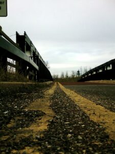 photo of what appears to be an abandoned industrial site--the photo draws the eye forward, towards the horizon down a long, unkempt road 