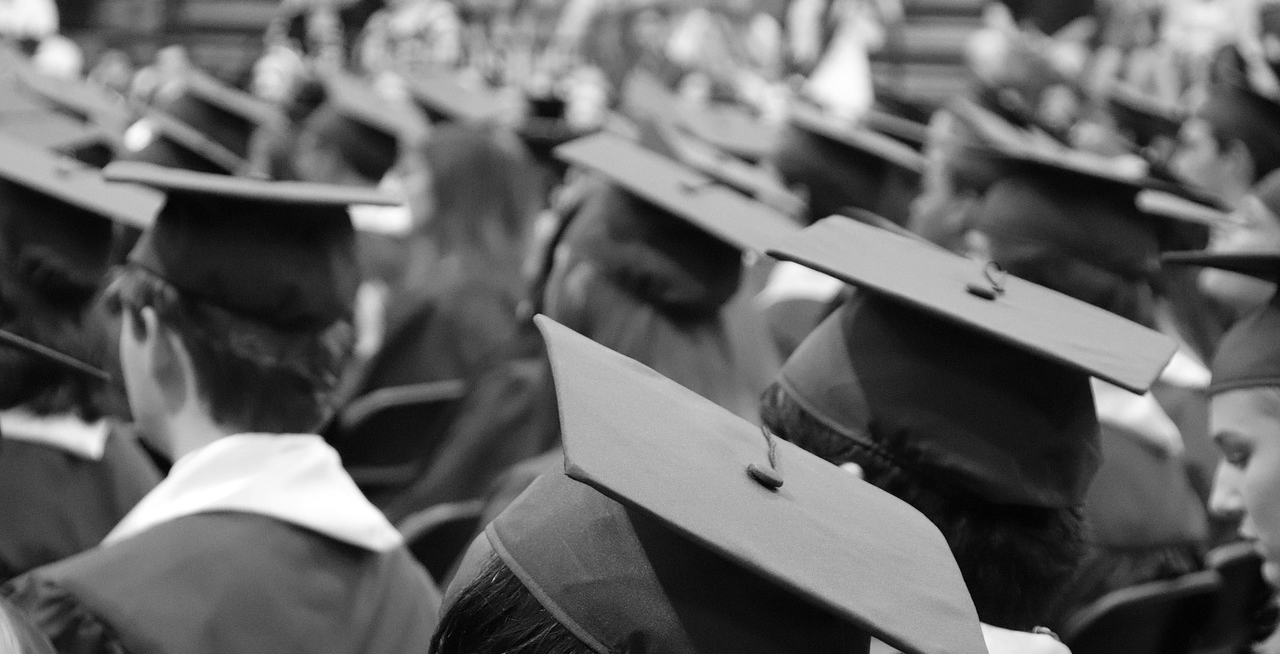 A black and white photo of people sitting with graduation caps on.