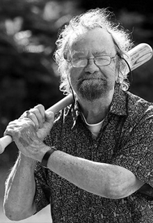 A black and white image of a white man smiling holding a baseball bat