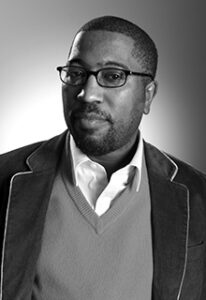 A black and white image of a black man wearing glasses