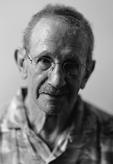 A black and white image of a white man in glasses staring into the camera