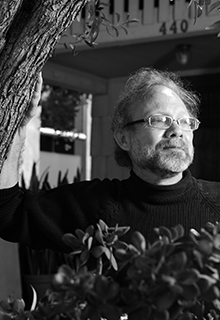 A black and white image of a man in front of a tree and bushes