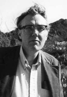 A black and white image of a white man with mountains in the background