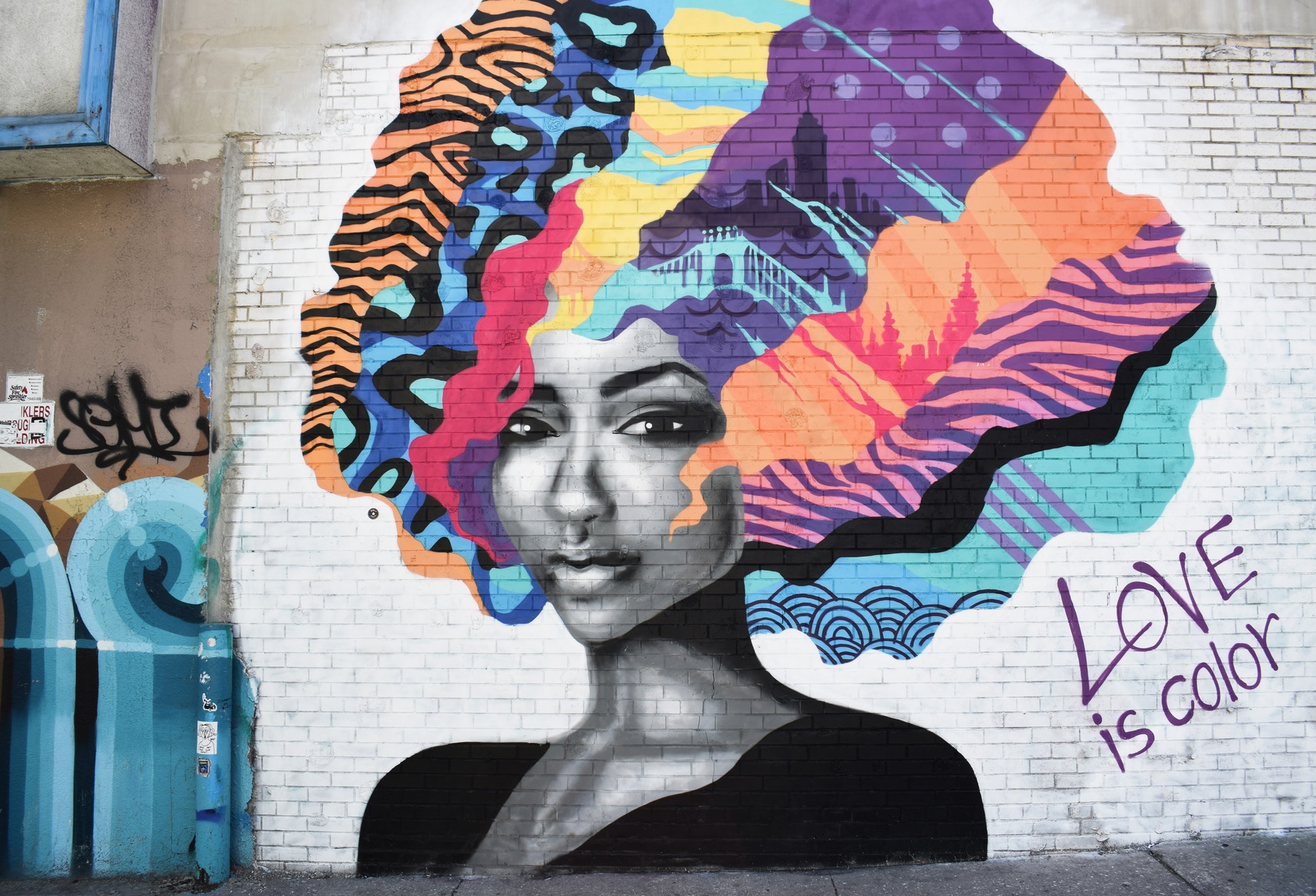 Woman with blue, purple, and pink hair mural on the side fo a white brick building