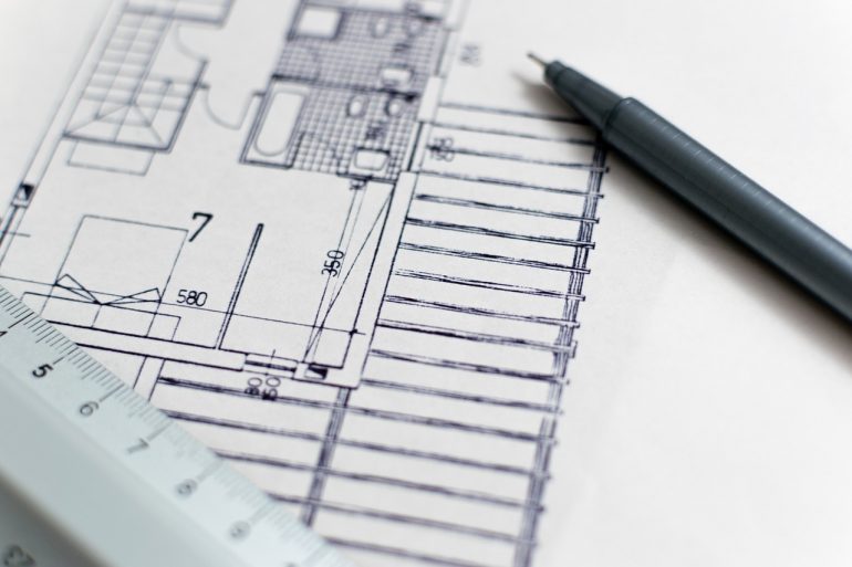 Picture of a pen-drawn house blueprint. On top of the blueprint lies a pen and a ruler. 