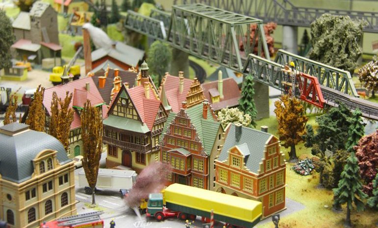 Picture of a colorful miniature city consisting of a couple of houses, bridges, trucks, and other buildings. 