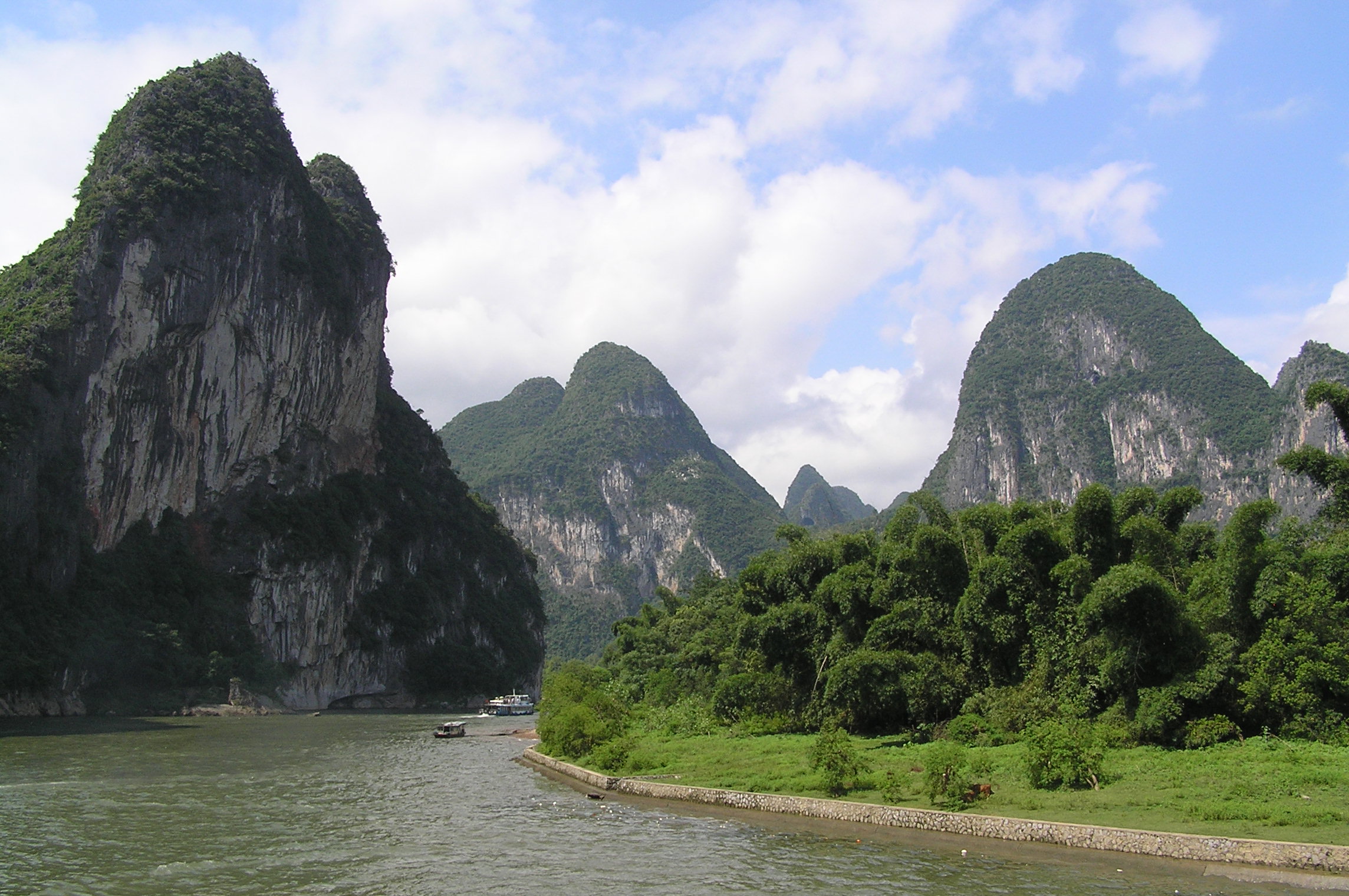 Picture of the Li river going through big mountains full of vegetation. A couple of small boats can be seen on the river.