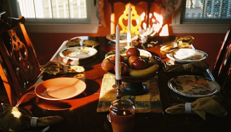 Picture of a set dinner table with candles, a fruit bowl, mantels, and silverware 