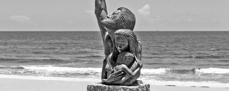Picture of a statue on a beach of three family members hugging each other