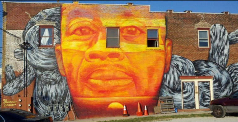 Mural on a brick wall of the face of a Black man. 