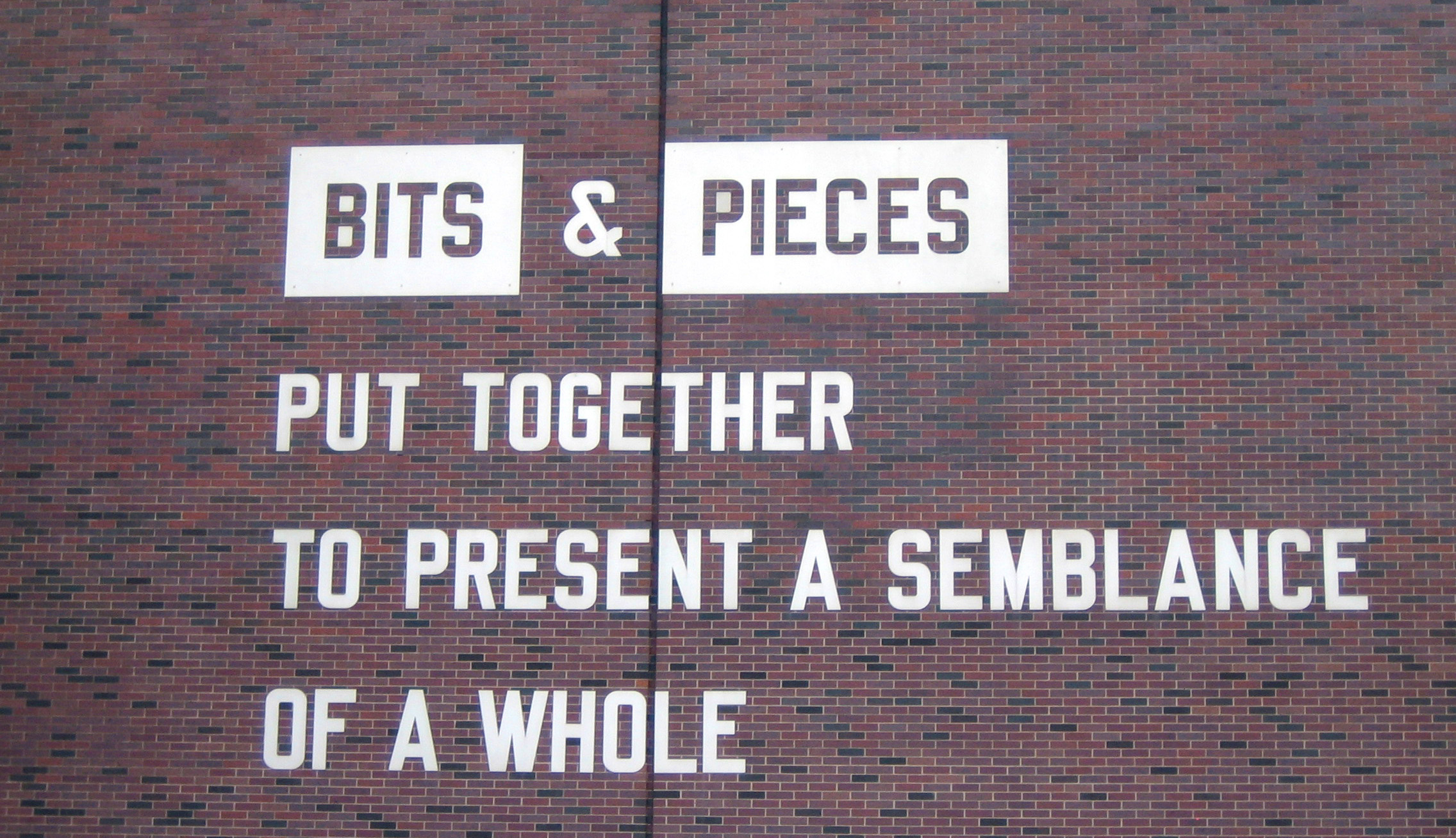 Brick wall with painted letters that read "Bits & Pieces put together to present a semblance of a whole."