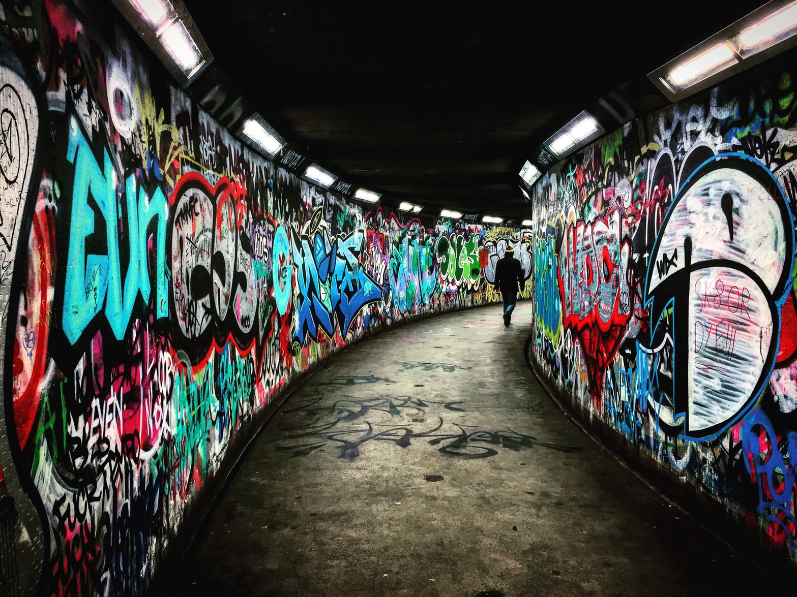 Man walking in tunnel with graffiti on the walls.