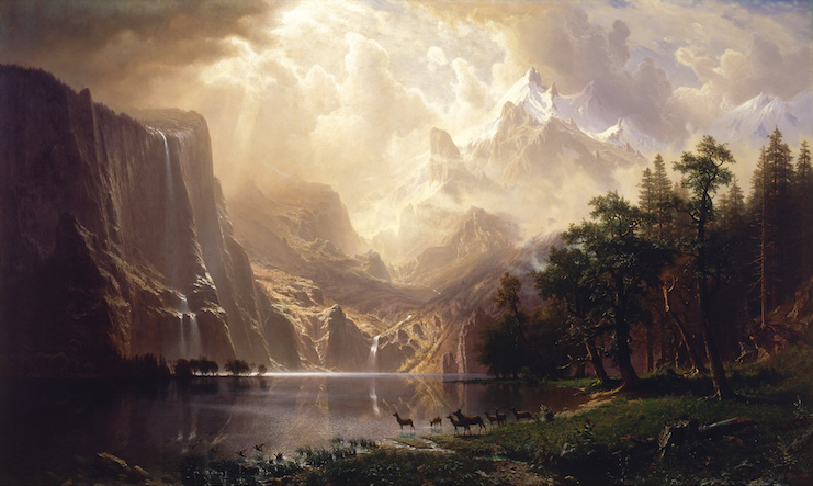 Serene landscape with sunlight shining over a forest, a lake, and a mountain.