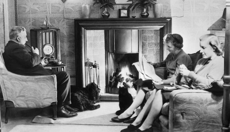 Man and two women sitting at a fireplace.