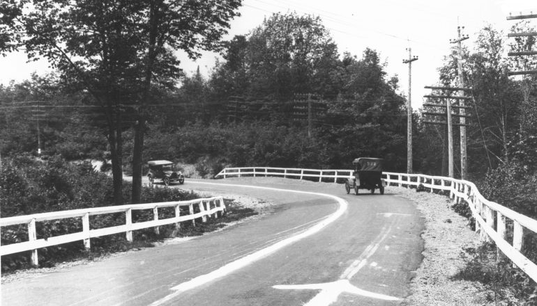 black and white photo of old cars driving on road