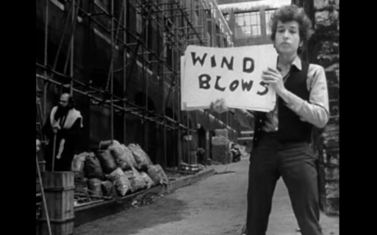 Clip of Bob Dylan's "Subterranean Homesick Blues" video of Bob Dylan holding up a handwritten sign reading "Wind Blows" in an alley