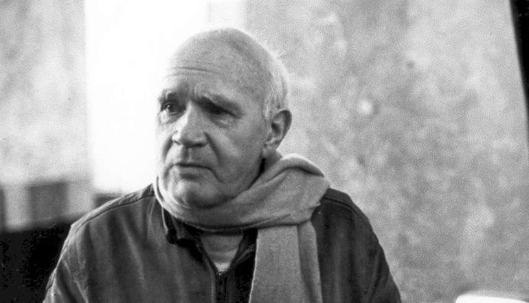 Old man wearing a scarf and leather jacket looking away from the camera.