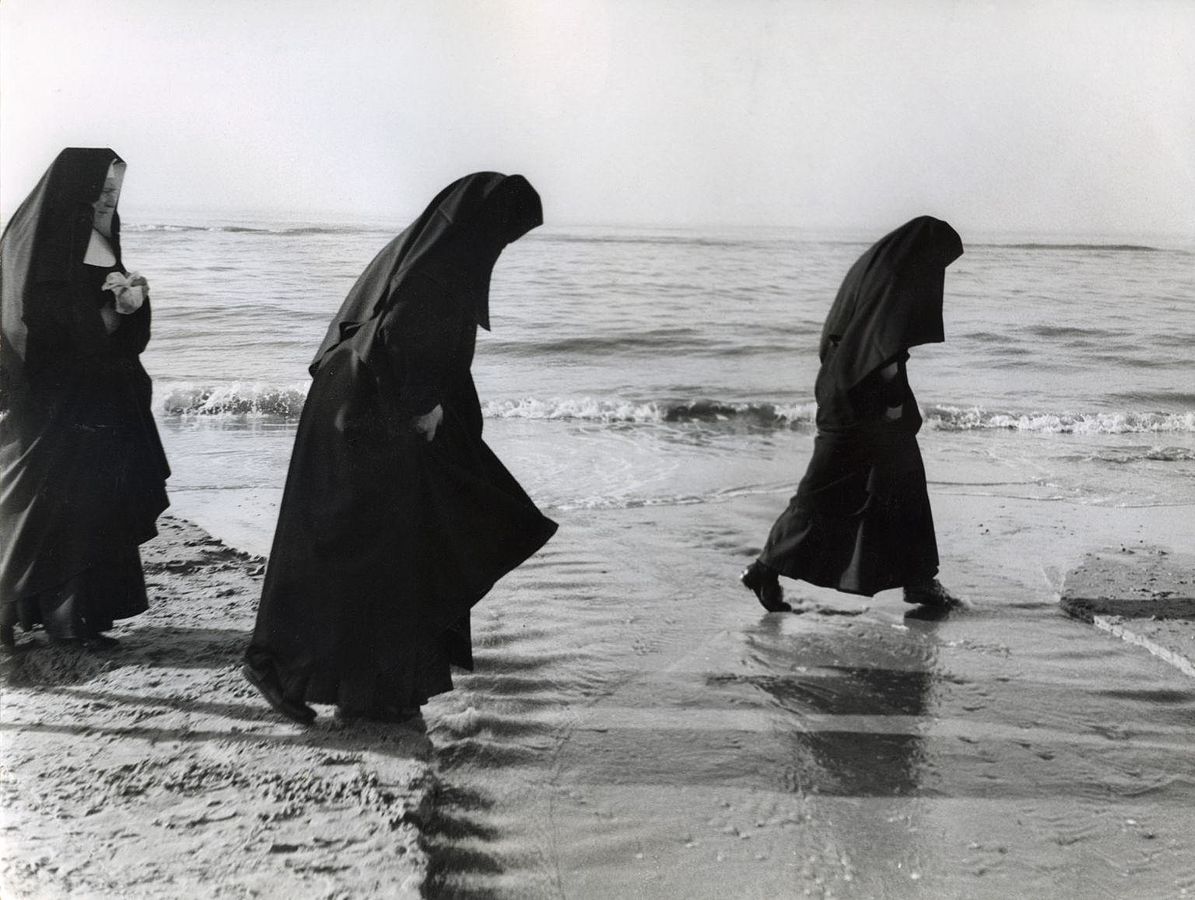 Nuns dressed in black robes walking on a beach.