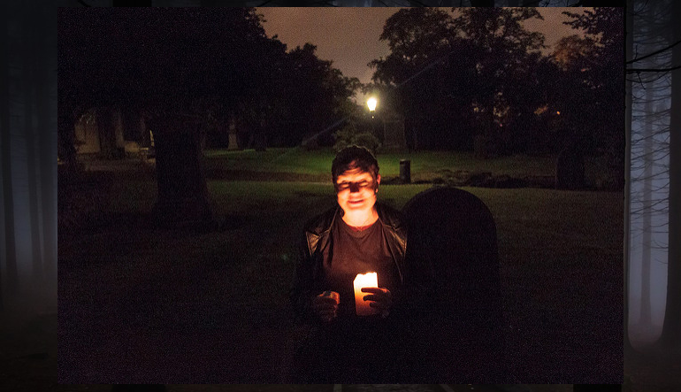 Person holding a candle and sitting outside at night.