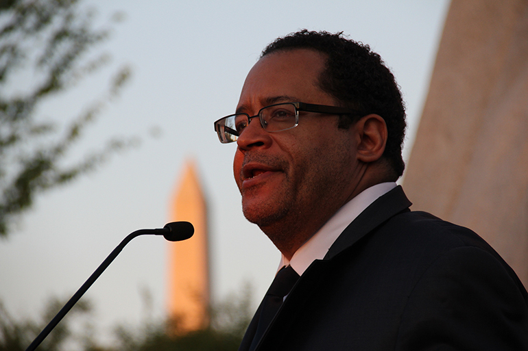 Man with glasses speaking into a microphone.