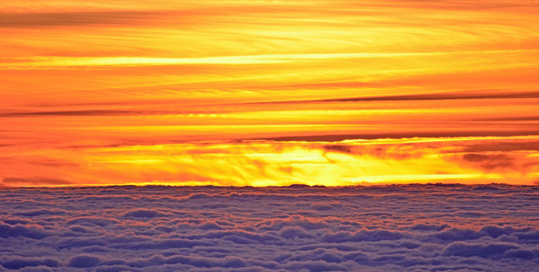 Orange sunset above fluffy clouds.