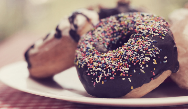 A plate of donuts, with a chocolate iced with rainbow sprinkles donut in focus.