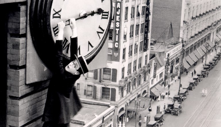 Man hanging from the hands of a large clock.