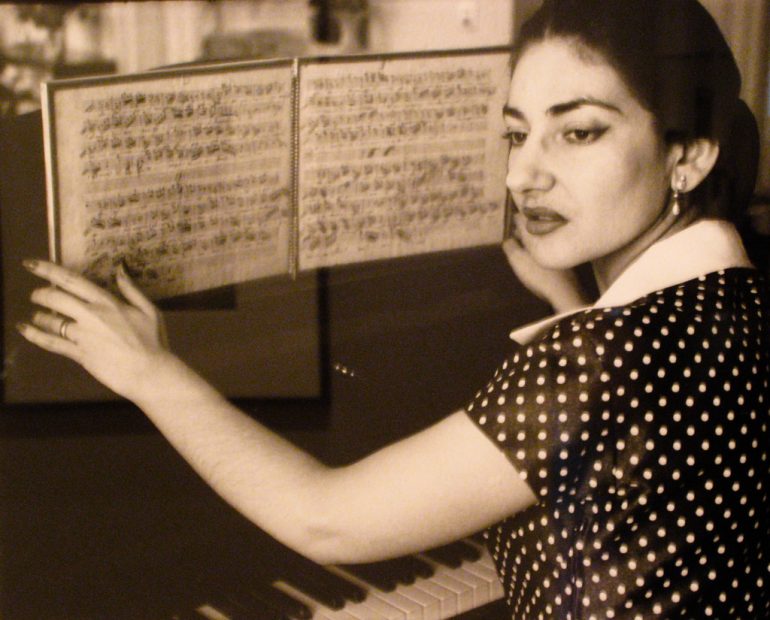 Old photograph of a woman holding open a music book above a piano.