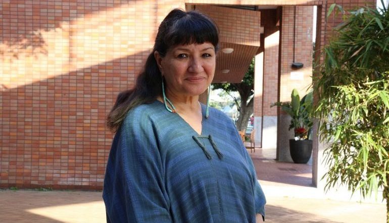 a photograph of Sandra Cisneros standing outdoors by a building