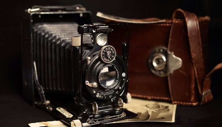 black view camera with brown case sitting on top of several vintage photographs