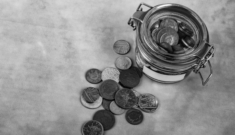 in black and white - glass tin of coins with coins scattered outside of it 