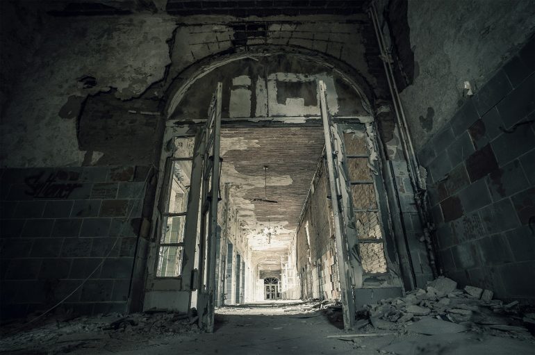 Image of an abandoned concrete building with a large open doorway with windowpanes.