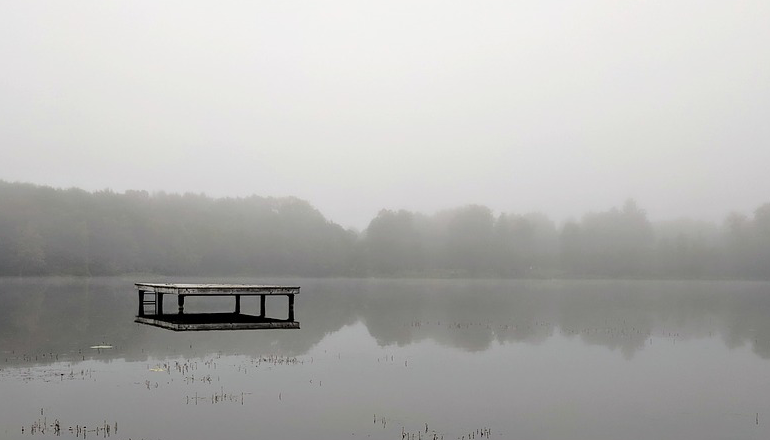 A lone dock sits in the middle of a grey, misty lake. 
