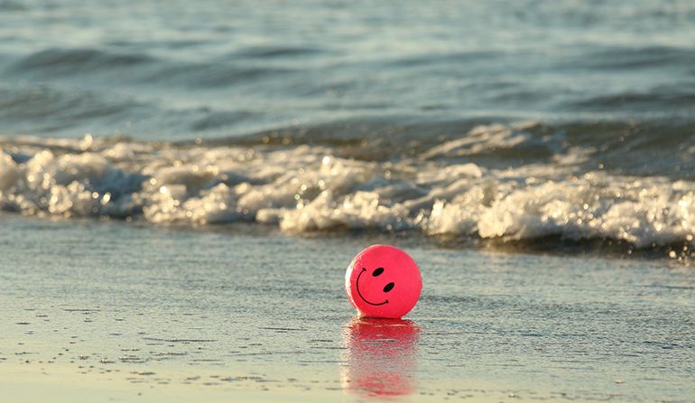 A beach ball with a smiley face painted on it sits on the beach 