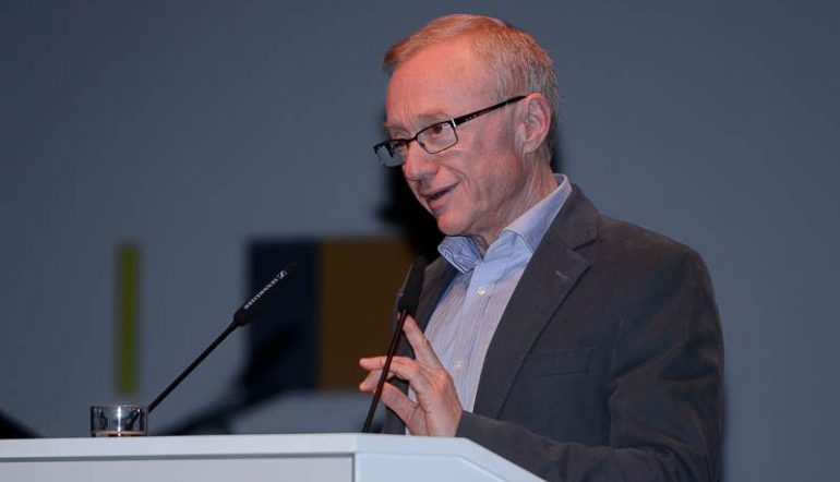 David Grossman standing behind a podium at a microphone speaking at an event