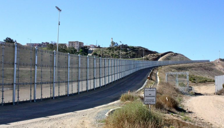 Fenced border between US and Mexico with a sign that reads "US Property, no trespassing"