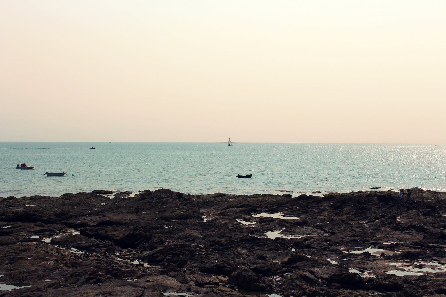 photograph of a rocky beach with sailboats in the distance