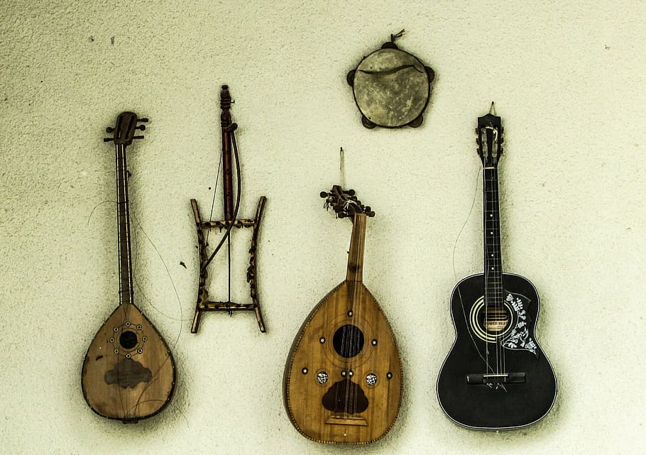 two wooden ouds hang against a pale green wall alongside a black ukulele 