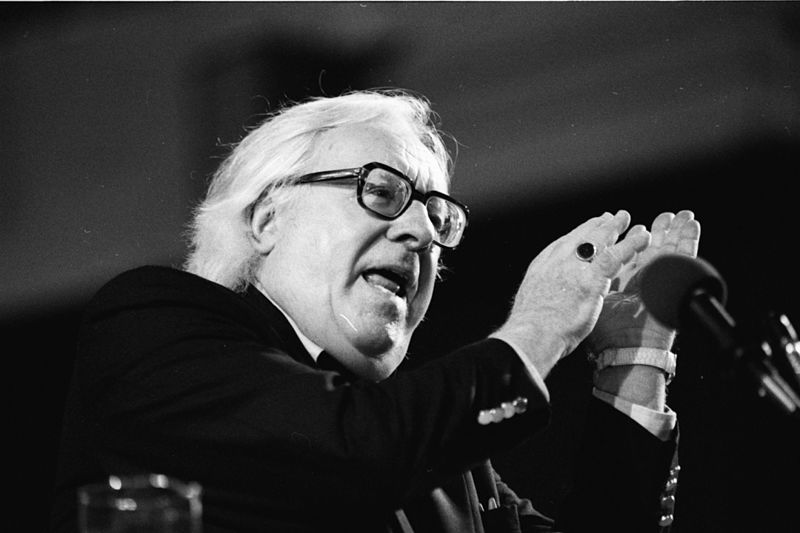 black and white photograph of Ray Bradbury, speaking at a microphone, with his hands gesturing upwards as he speaks 