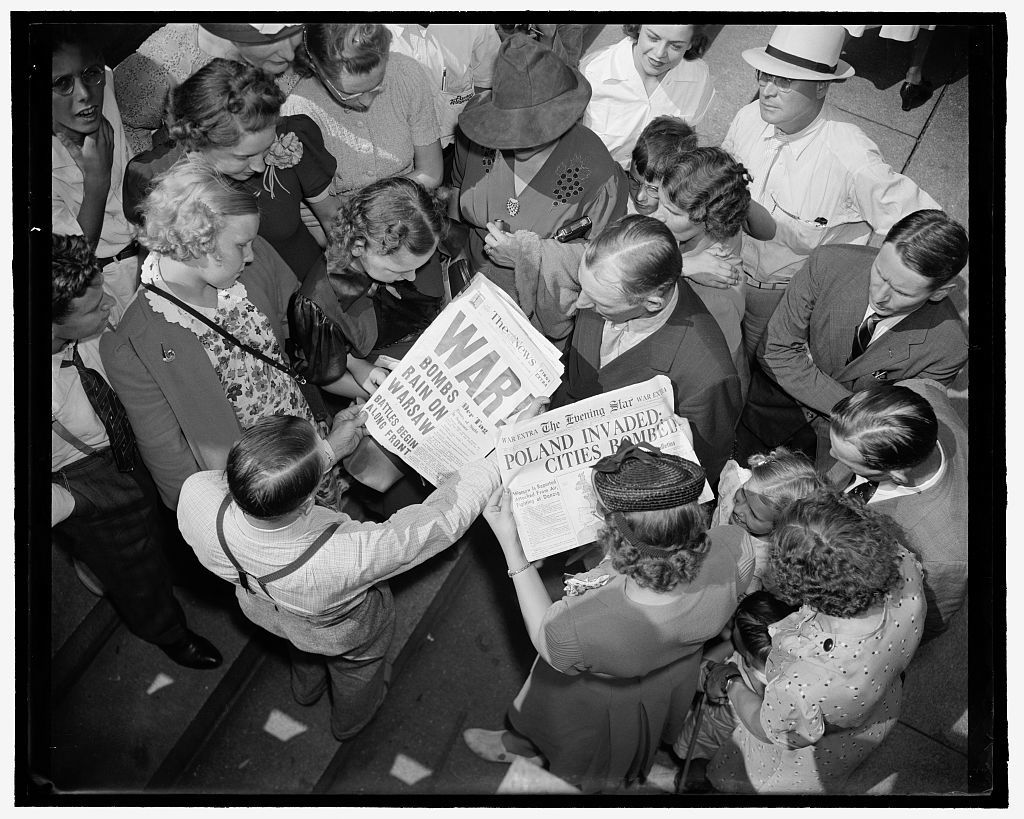 a black and white photograph of a crowd of people looking at a newspaper that says WAR