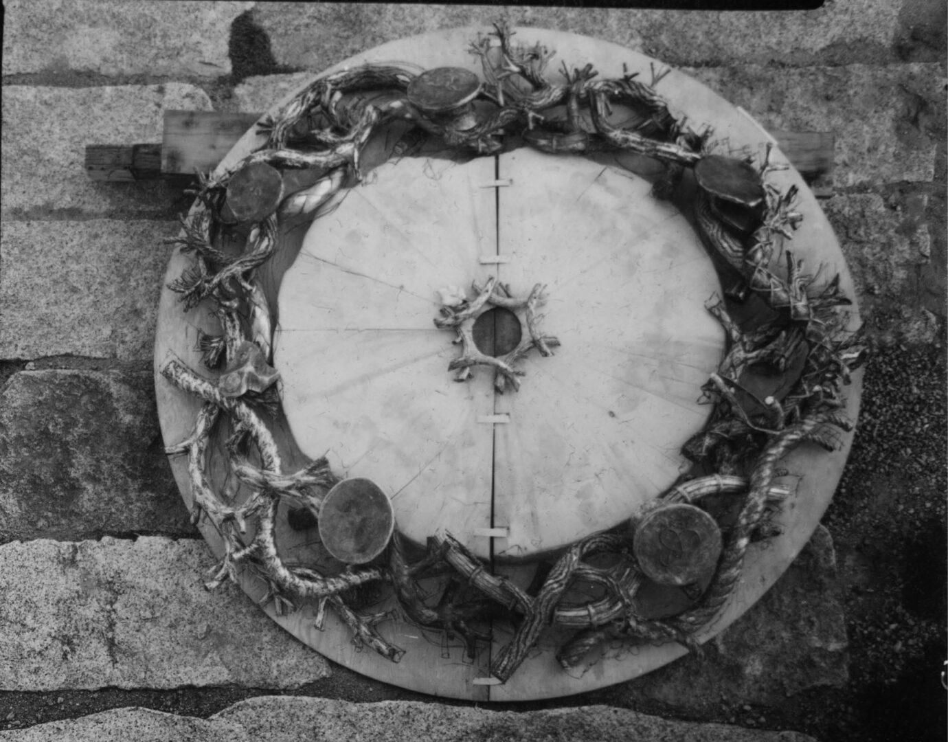 Circular wreath with intertwined branches and military hats on a stone surface.