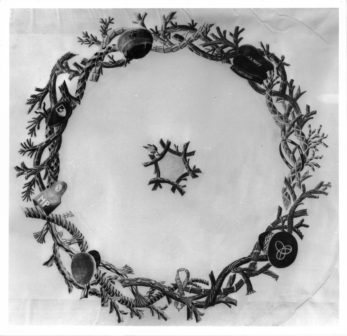 An image of a decorative wreath with military symbols and insignias in black and white.