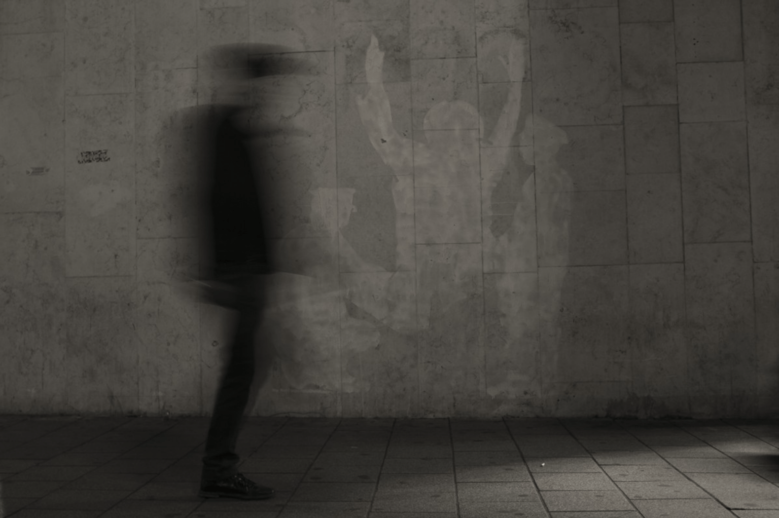 Black and white blurry photograph of a person standing against a cement wall