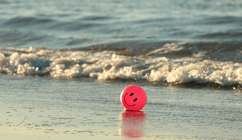 A beach ball with a smiley face painted on it sits on the beach A picture of a ball with a smiley face on the ocean.
